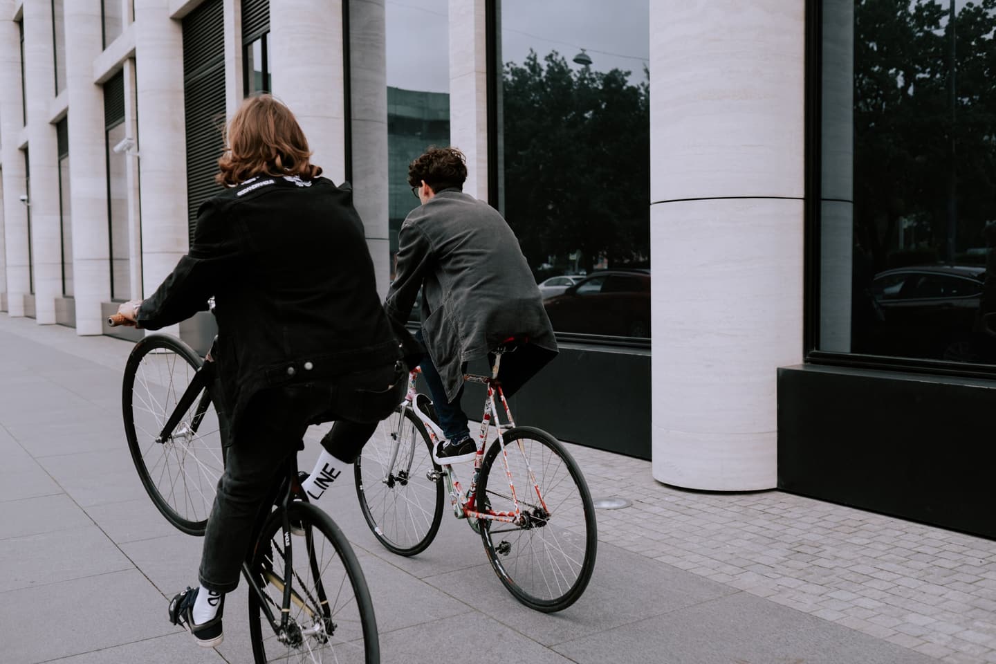 Two students cycling past a modern campus building