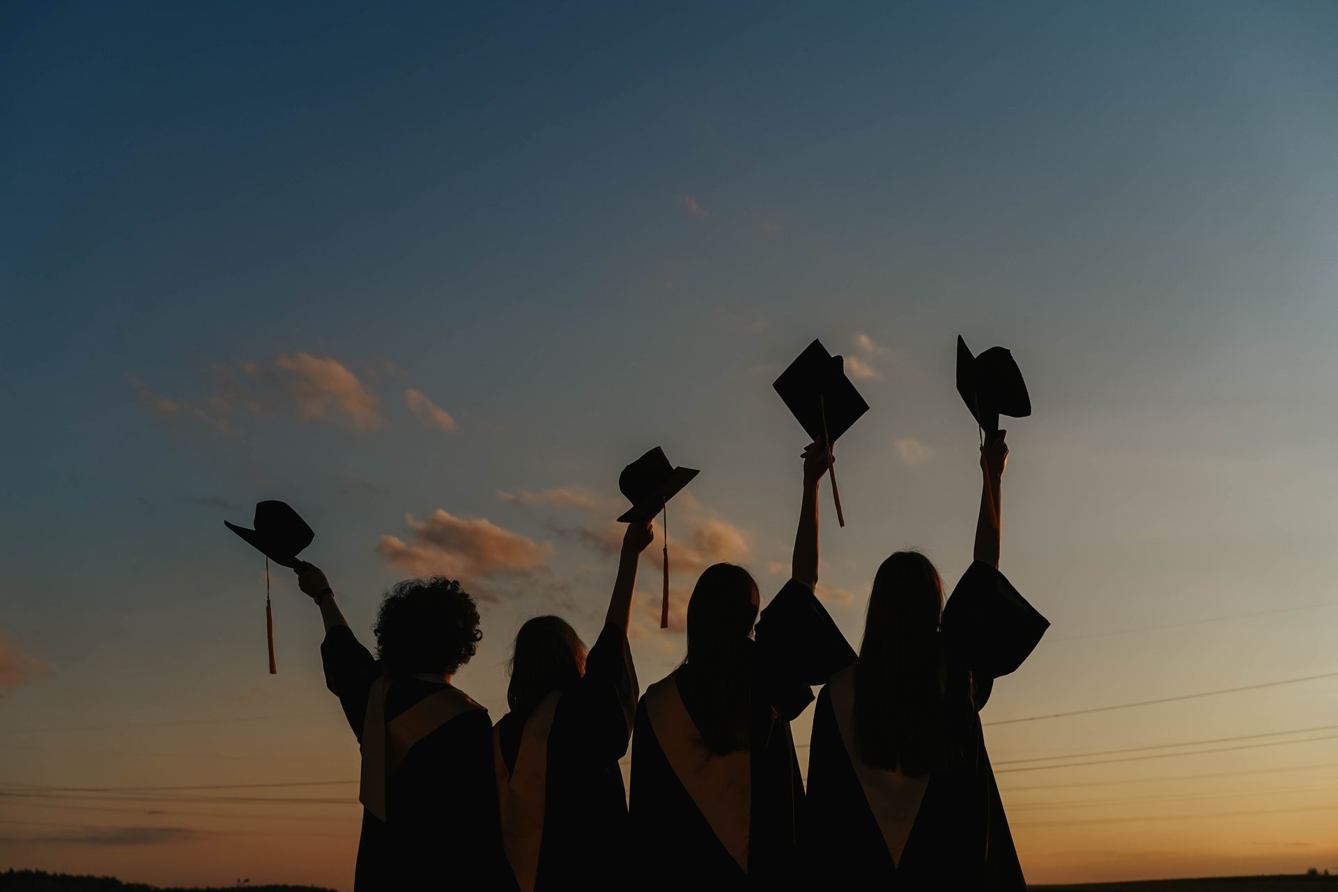 Graduates raising their caps against a dusk sky